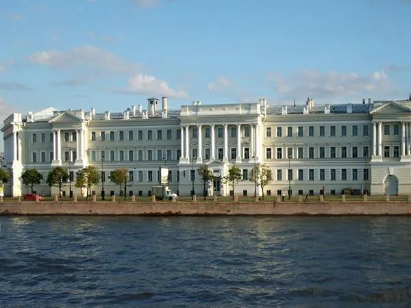Здание Санкт-Петербургского государственного университета на набережной Невы. Историческое светло-серое здание с колоннами в классическом стиле на фоне голубого неба